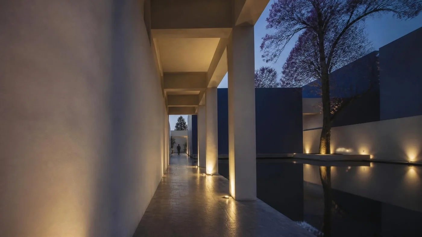 Pasillo de arquitectura contemporánea con espejo de agua y jacaranda al anochecer